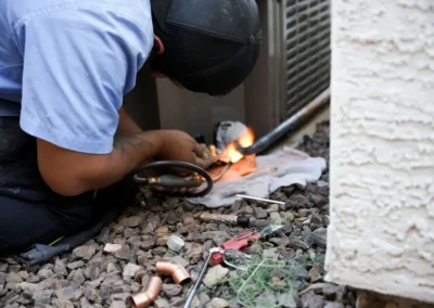 HVAC technician brazing refrigerant lines on an outdoor AC unit in Mesa, AZ